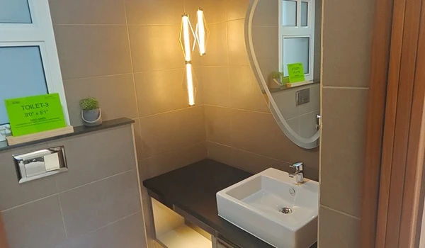 Modern bathroom (Toilet-3) at Nambiar District 25 4 BHK model flat, featuring a sleek vessel sink, organic-shaped backlit mirror, and designer pendant lighting