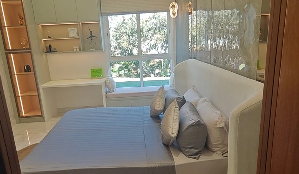Modern Bedroom 2 at Nambiar District 25 4 BHK model flat, featuring a cozy window seat overlooking the garden, an integrated study desk, and illuminated display shelving