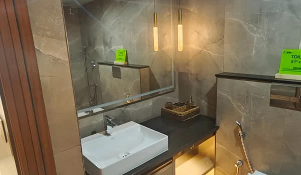Luxurious master bathroom vanity in Nambiar District 25 4 BHK model flat, featuring a wide mirror, designer pendant lights, grey stone-finish tiles, and a premium vessel sink