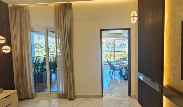 Interior view of the master bedroom in Nambiar District 25 4 BHK model flat, showing the balcony access, pendant lighting, and the doorway leading to the main living area