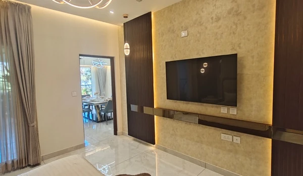 View of the master bedroom TV wall in Nambiar District 25 4 BHK model flat, featuring textured wallpaper, ambient backlighting, and a clear sightline into the dining area