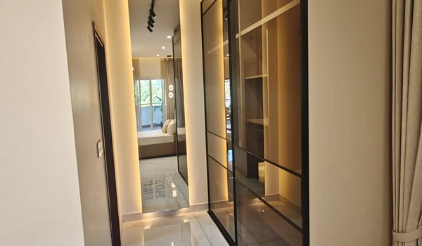 Walk-in wardrobe area in the master bedroom of Nambiar District 25 4 BHK model flat, featuring floor-to-ceiling tinted glass wardrobes with internal lighting and a full-length dressing mirror