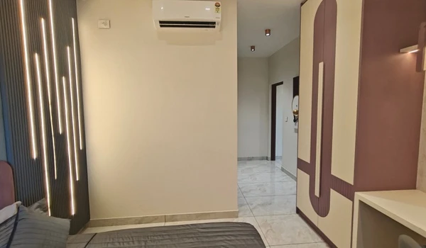 Interior view of a modern bedroom at Nambiar District 25 model flat, showing a sleek wardrobe with purple accents, a minimalist study desk, and integrated vertical LED wall lighting