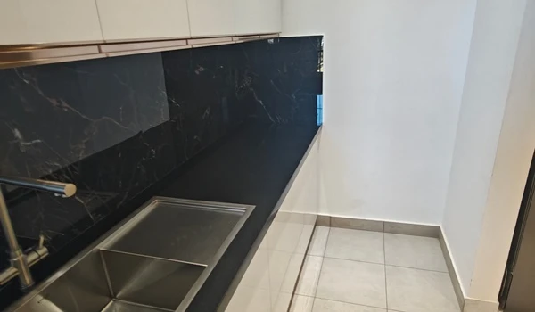 Modern kitchen utility area at Nambiar District 25 featuring a sleek black granite countertop, stainless steel double-bowl sink, and premium black marble backsplash with gold veining