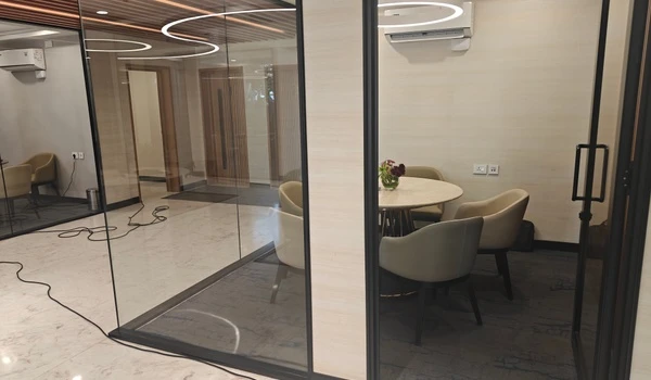 Close-up view of a glass-enclosed private meeting room at Nambiar District 25 sales gallery, featuring a round table, comfortable seating, and modern interiors