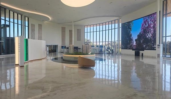Wide-angle interior view of Nambiar District 25 sales gallery featuring a large LED screen, central architectural model, and luxurious marble flooring